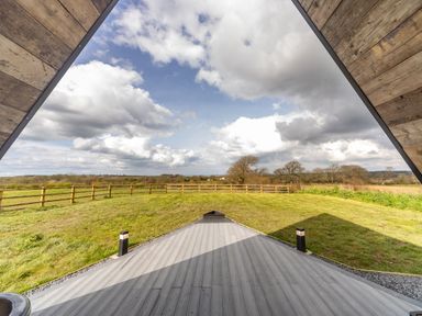 A wooden deck overlooking a fenced grassy field with trees and a cloudy sky at The Tri-Pod in Pantcefn near Llanarth