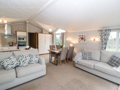 An open living space with two sofas, a dining table with chairs, and a kitchen area at No.7 Skiddaw View Moota near Aspatria