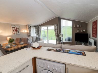 A living room with a dining table set beside a beige sofa and a television at No.7 Skiddaw View in Moota near Aspatria