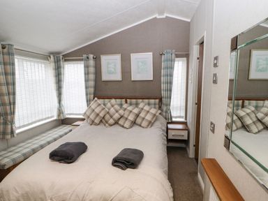 A bedroom with a bed with plaid pillows and curtains next to windows and nightstands at No.7 Skiddaw View Moota near Aspatria