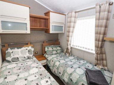A bedroom with two single beds with sheep patterned bedding and plaid curtains at No.7 Skiddaw View Moota near Aspatria