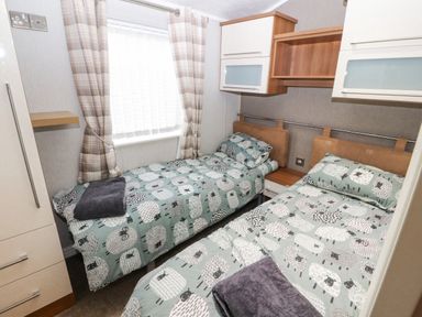 A bedroom with two single beds with sheep patterned bedding and curtains at No7 Skiddaw View Moota near Aspatria