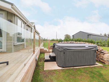 An outdoor hot tub with steps next to a wooden deck and a house at No 7 Skiddaw View in Moota near Aspatria