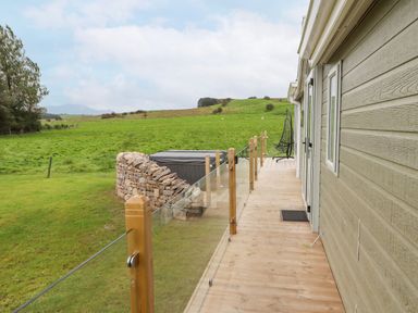 A wooden deck beside a house with glass railing overlooking a grassy field at No.7 Skiddaw View in Moota near Aspatria