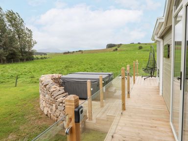 A wooden deck with glass railing and a covered hot tub beside a grassy field at No.7 Skiddaw View Moota near Aspatria