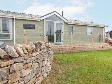 A single-story house with a stone wall in front and a wooden deck with glass railing at No.7 Skiddaw View in Moota near Aspatria