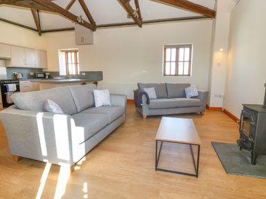 A living room with two grey sofas a wooden coffee table a wood stove and an open kitchen at The Granary in Prussia Cove near Rosudgeon