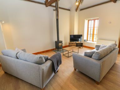 A living room with two grey sofas a wood burning stove a coffee table and a television at The Granary in Prussia Cove near Rosudgeon