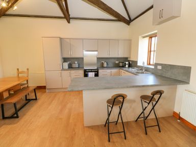 A kitchen with a breakfast bar and two stools next to a dining table with bench seating at The Granary in Prussia Cove near Rosudgeon