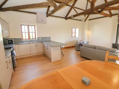 An open plan kitchen and living area with wooden beams a dining table kitchen cabinets and grey sofas at The Granary in Prussia Cove near Rosudgeon