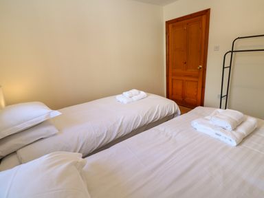 A bedroom with two single beds made with white linens and towels on each bed at The Granary in Prussia Cove near Rosudgeon