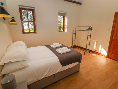 A bedroom with a double bed towels on the bed two windows and a clothes rack at The Granary in Prussia Cove near Rosudgeon