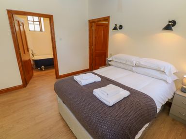 A bedroom with a double bed and folded towels with an open door revealing a bathroom with a bathtub at The Granary in Prussia Cove near Rosudgeon