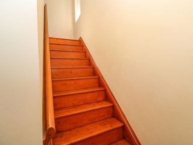A wooden staircase with a handrail and light colored walls at The Granary in Prussia Cove near Rosudgeon