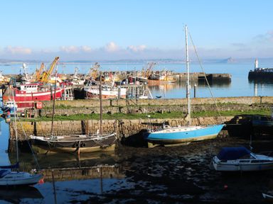 A harbor with boats docked near stone walls and calm water at The Granary in Prussia Cove near Rosudgeon