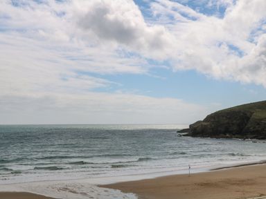 A beach with waves and rocky cliffs under a partly cloudy sky at The Granary in Prussia Cove near Rosudgeon