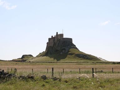 A hilltop castle in a rural field with fences and grassy terrain at Kits Cottage in Middleton near Belford