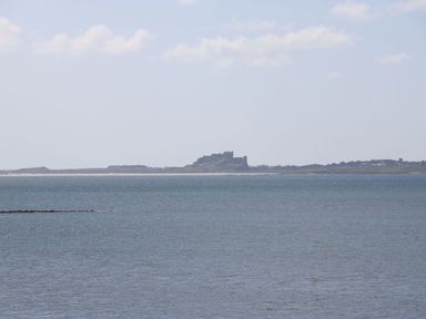 A body of water with a shoreline and a castle in the distance at Kits Cottage in Middleton near Belford