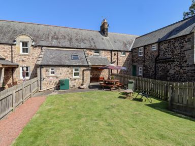A garden with grass and patio furniture at Kits Cottage in Middleton near Belford