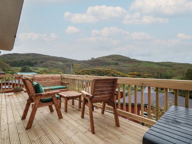 A wooden deck with outdoor furniture overlooking green hills at Y Goedlan in Tywyn