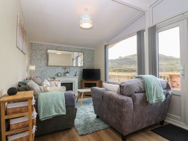 A living room with two sofas a television on a wooden cabinet a coffee table and large windows showing an outdoor view at Y Goedlan in Tywyn