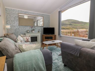 A living room with sofas a coffee table a television and a large window showing a hill at Y Goedlan in Tywyn