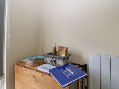 A wooden table with a basket containing a wine bottle and snacks and a blue guest information booklet at Y Goedlan in Tywyn
