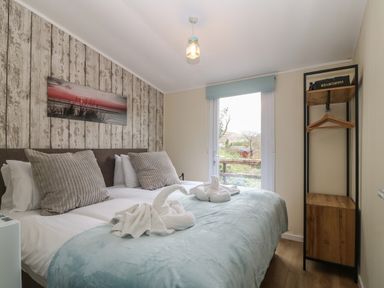 A bedroom with a double bed pillows towel swans painting on wall and a shelving unit at Y Goedlan in Tywyn