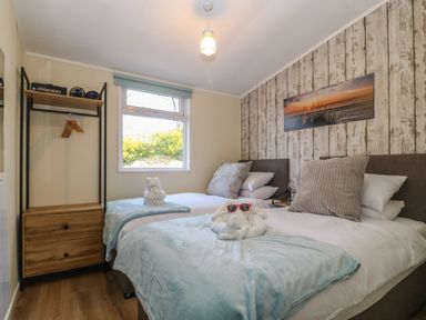 A bedroom with two single beds a window with a view of bushes and a wooden wardrobe at Y Goedlan in Tywyn