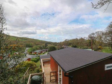 A view of multiple red buildings with dark roofs surrounded by trees and hills at Y Goedlan in Tywyn