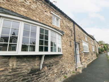 A stone building with white framed windows and a white door along a sidewalk at York House in Thornton Dale