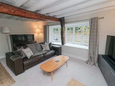 A living room with a leather sofa a wooden coffee table a piano and a large window at York House in Thornton Dale