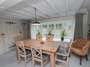 A dining room with a wooden table and six chairs next to a window with three plants York House Thornton Dale