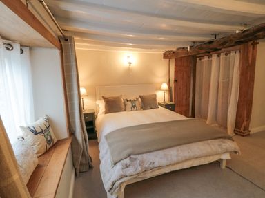 A bedroom with a bed with pillows and blankets two bedside tables with lamps wooden beams and curtains at York House in Thornton Dale