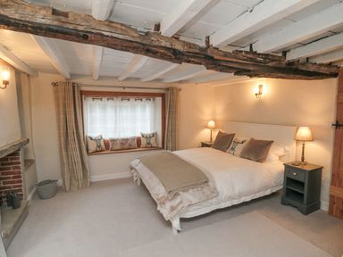 A bedroom with a bed and two bedside tables with lamps next to a window seat with cushions at York House in Thornton Dale