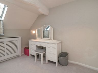 A white dressing table with a mirror and stool next to a window and two laundry baskets at York House in Thornton Dale