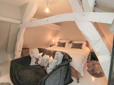 A bedroom with a double bed bedside tables and a sofa with cushions under exposed white beams