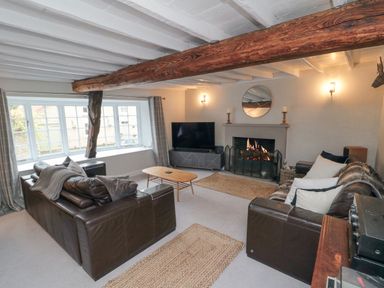 A living room with two leather sofas a wooden coffee table a fireplace a TV and exposed wooden beams at York House in Thornton Dale