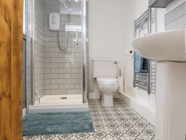 A bathroom with a shower, toilet, sink, towel rail and patterned floor tiles at Quarry Cottage in Bethesda