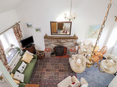 An overhead view of a living room with a brick fireplace a green sofa with cushions a television on a wooden stand a dining table with chairs and a hanging chandelier at Quarry Cottage in Bethesda