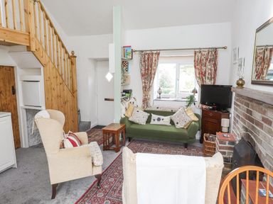A living room with armchairs a green sofa a brick fireplace TV and window with floral curtains at Quarry Cottage in Bethesda