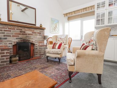 A room with two armchairs a brick fireplace a wooden table and kitchen cabinets at Quarry Cottage in Bethesda