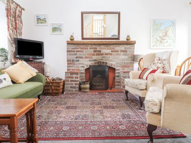 A living room with a brick fireplace two armchairs a green sofa a wooden coffee table a television and framed pictures at Quarry Cottage in Bethesda