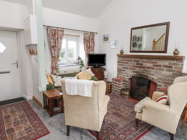 A living room with chairs a fireplace a television and patterned rugs at Quarry Cottage in Bethesda