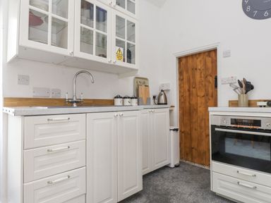 A kitchen with white cabinets a wooden door a stainless steel kettle and an oven at Quarry Cottage in Bethesda