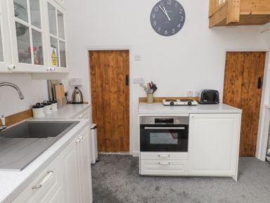A kitchen with white cabinets a sink a wall clock and wooden doors at Quarry Cottage in Bethesda