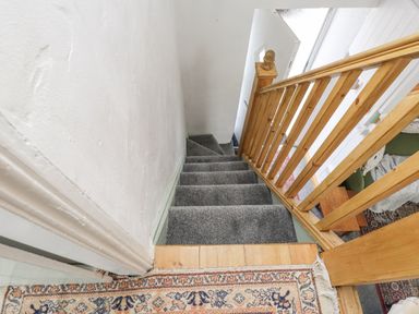 A staircase with gray carpet and wooden railing overlooking a living room at Quarry Cottage in Bethesda