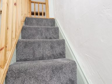 A staircase with grey carpet and wooden railing at Quarry Cottage in Bethesda