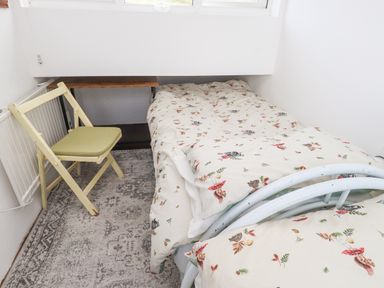 A small bedroom with a single bed a folding chair a small wooden desk and a patterned rug at Quarry Cottage in Bethesda