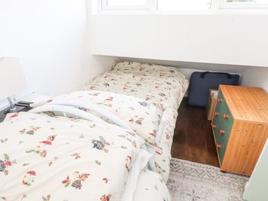 A small bedroom with two single beds under a sloped ceiling a wooden chest of drawers and a blue suitcase on a wooden floor at Quarry Cottage in Bethesda